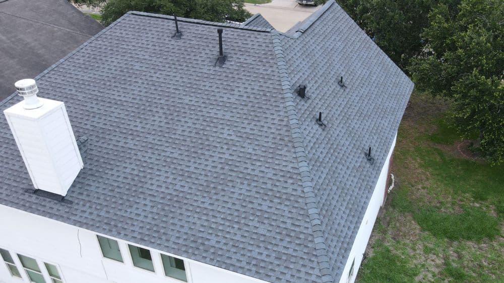 Aerial view of a modern house roof with dark shingles and multiple vent pipes.