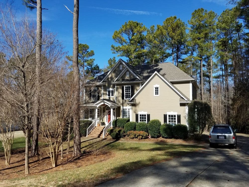 Elegant two-story house with landscaped yard and tall trees under a clear blue sky.
