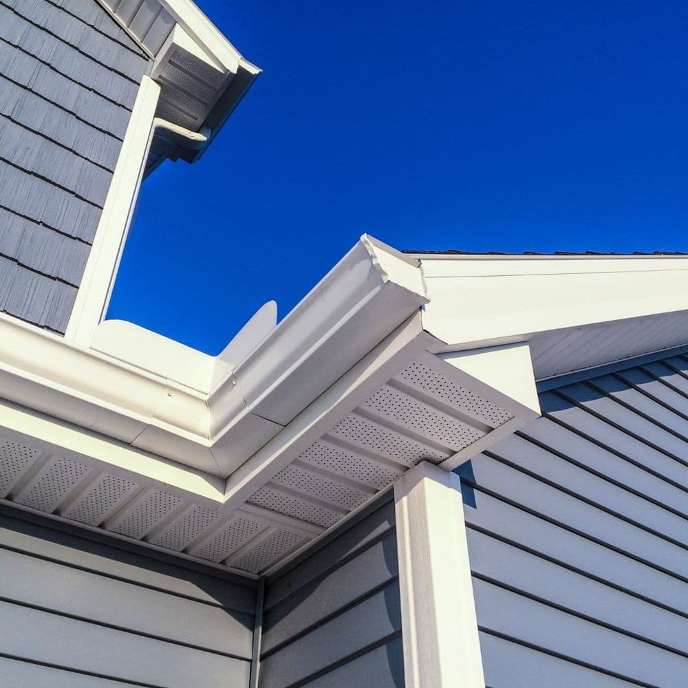 Close-up of a grey house exterior with white gutters against a blue sky.