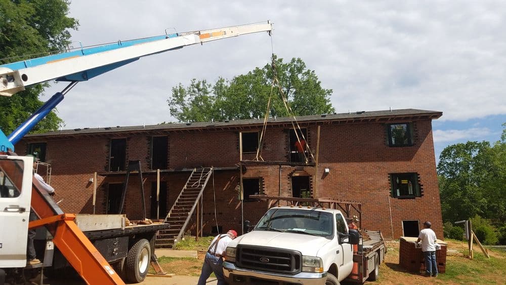 Construction workers using a crane to renovate a brick apartment building.