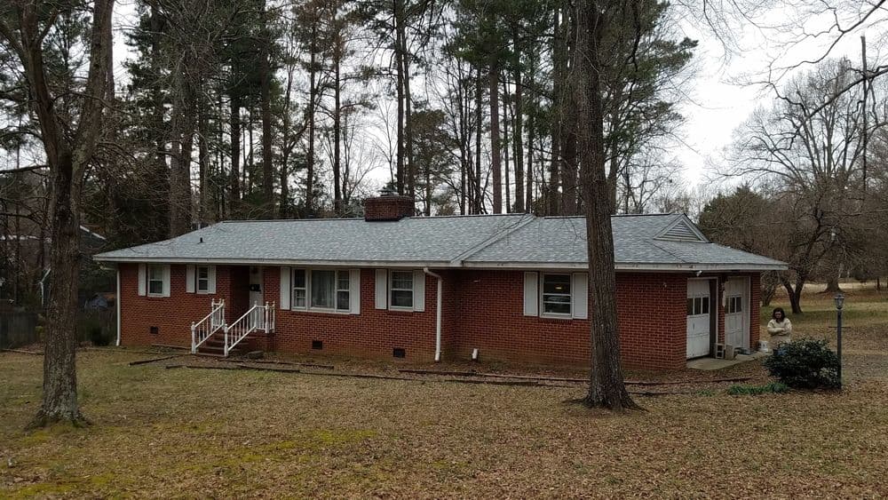 Brick ranch-style house surrounded by trees and grassy yard in a serene setting.
