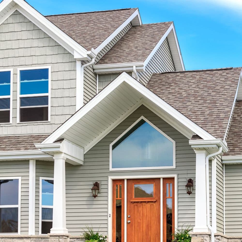 Modern gray house exterior with a wooden front door and large windows under a clear blue sky.