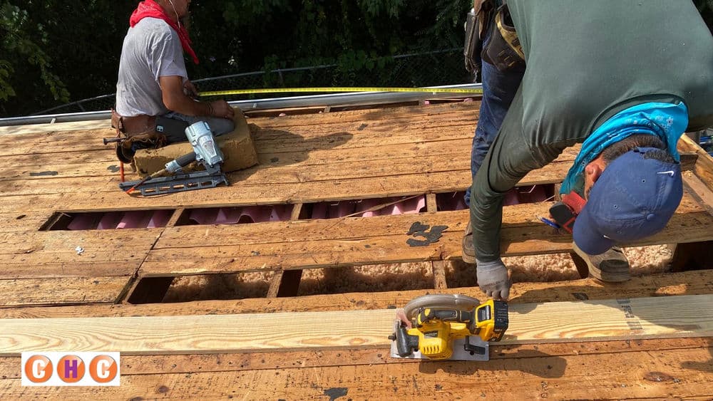 Roofing workers installing plywood on a residential home, focusing on construction and safety.